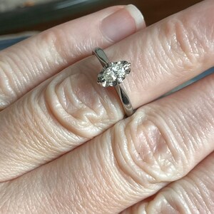 Puede incluir: Un anillo de plata con un solo diamante redondo y transparente engastado en garras.
