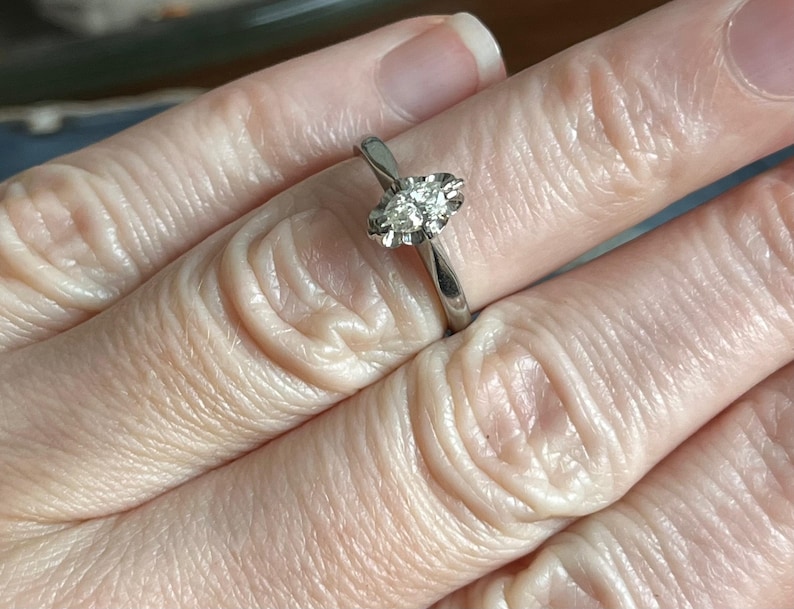 Puede incluir: Un anillo de plata con un solo diamante redondo y transparente engastado en garras.