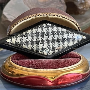 May include: A black and white houndstooth patterned brooch in a black resin setting. The brooch is displayed in a red velvet lined, gold and red ring box.