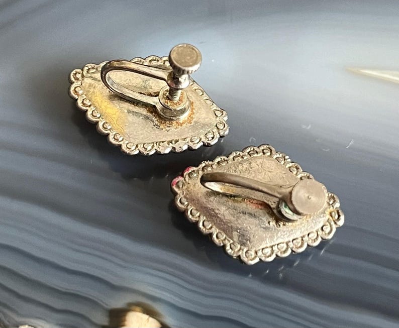 May include: A pair of silver-tone clip-on earrings with a decorative, scalloped edge. The earrings have a silver-tone finish and a clip-on closure.