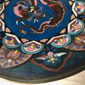 May include: A round, blue and white ceramic plate with a colorful dragon design in the center. The plate has a decorative border of flowers and geometric shapes.