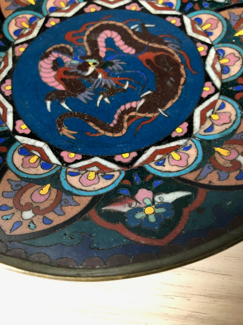 May include: A round, blue and white ceramic plate with a colorful dragon design in the center. The plate has a decorative border of flowers and geometric shapes.