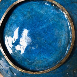 May include: A blue ceramic plate with a brass rim. The plate has a crackled glaze and a glossy finish.