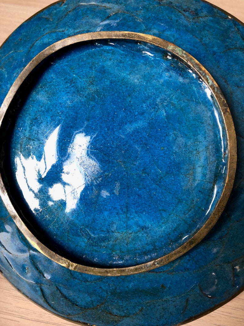 May include: A blue ceramic plate with a brass rim. The plate has a crackled glaze and a glossy finish.