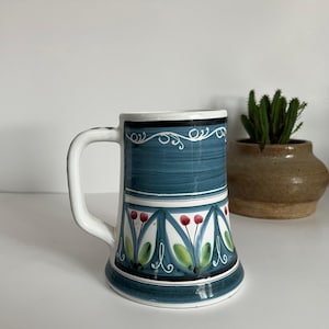 Puede incluir: Una taza de cerámica azul y blanca con un diseño floral. La taza tiene un asa blanca y una base azul.