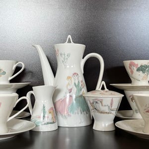 May include: A vintage white porcelain tea set with a decorative design. The set includes a coffee pot, creamer, sugar bowl, and several teacups and saucers. Each piece features a colorful illustration of women in dresses. The set is ideal for serving tea or coffee.