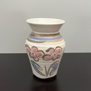 Może przedstawiać: Zestaw trzech ceramicznych kubków z nakrapianym, matowym wykończeniem. Kubki są w odcieniach kremu, jasnoszarym i ciemnoszarym. Każdy kubek ma prosty, minimalistyczny design i zaokrąglony uchwyt.