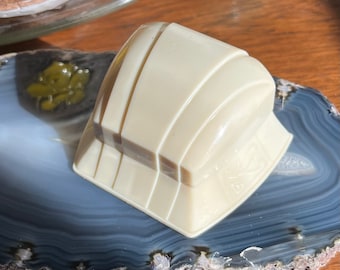 May include: A white ring holder with a geometric design. The holder is made of plastic and has a smooth, glossy finish. It is sitting on a blue and white agate slice.
