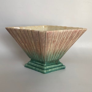 May include: A square ceramic planter with a pink and green glaze. The planter has a wide, flared opening and a stepped base.