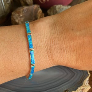 May include: A silver bracelet featuring blue and green opal-like segments. The bracelet is segmented with silver connectors. The bracelet is on a wrist.