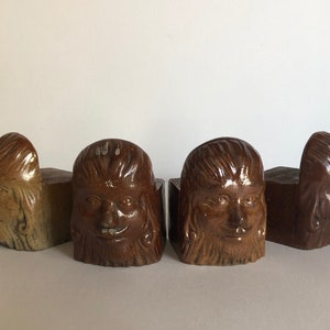 May include: Set of four brown ceramic bookends, each featuring a sculpted face with detailed hair and facial features. The bookends are rectangular and have a rustic, aged appearance, perfect for a home library or office space.