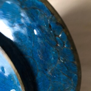 May include: Close-up of a blue ceramic bowl with a crackled glaze. The bowl has a dark blue rim and a light blue interior.