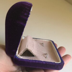 May include: A purple velvet jewelry box with a hinged lid and a white interior. The box has two compartments for storing earrings.