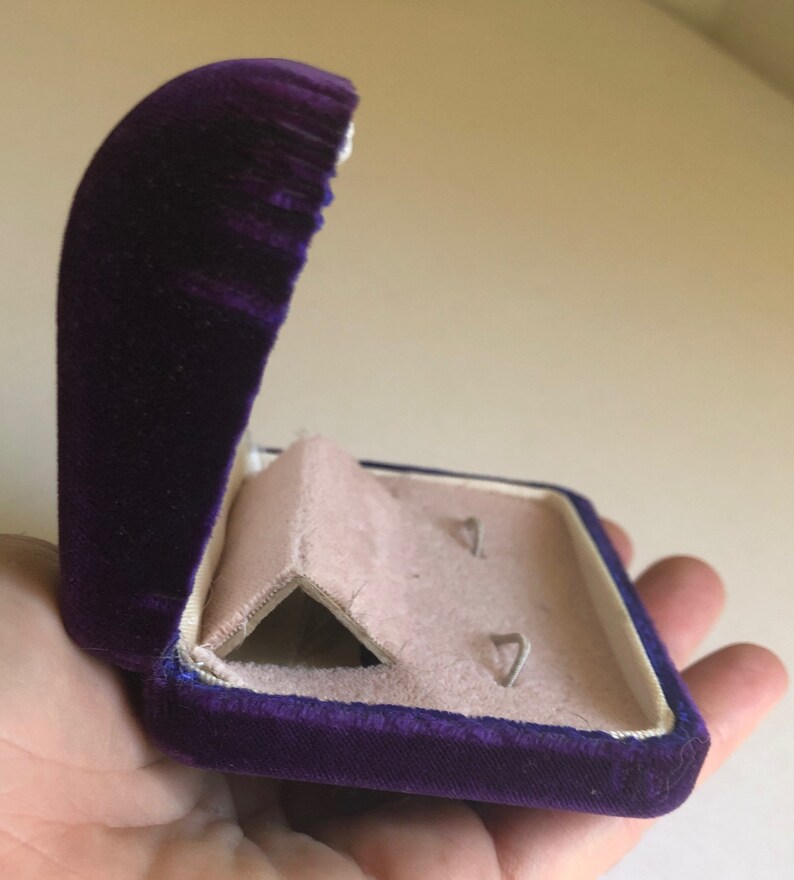May include: A purple velvet jewelry box with a hinged lid and a white interior. The box has two compartments for storing earrings.