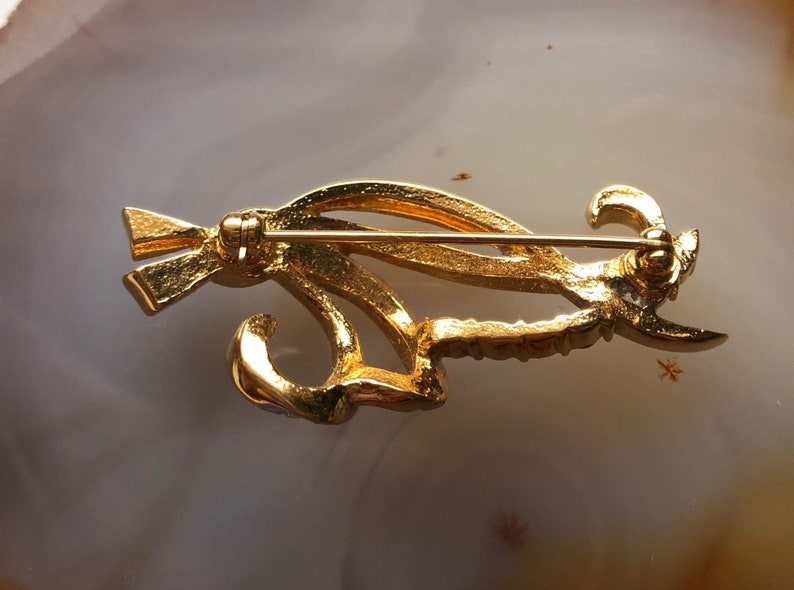 May include: Gold-toned brooch with a stylized design featuring a bird with a long tail. The brooch has a pin and catch closure on the back.