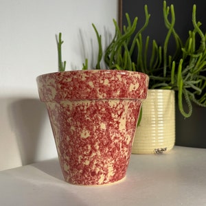 May include: A red and cream speckled ceramic planter with a rounded bottom and a wide rim.