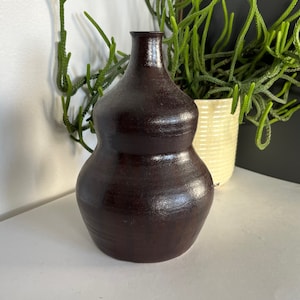 May include: A dark brown ceramic vase with a rounded, bulbous shape. The vase has a smooth, glossy finish and a slightly textured surface.