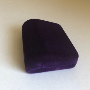 May include: A small, purple velvet box with a slightly curved top.