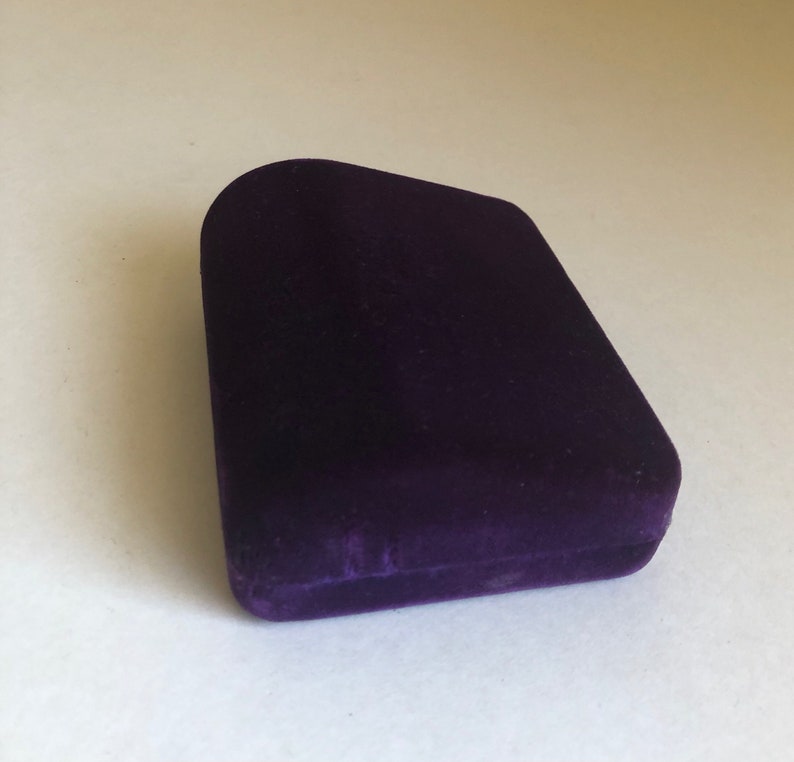 May include: A small, purple velvet box with a slightly curved top.