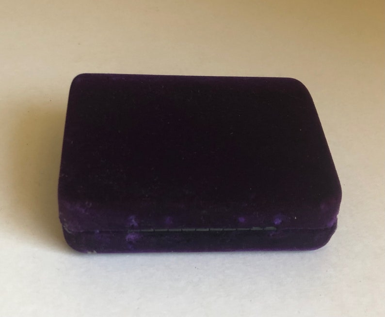 May include: A small, rectangular, purple velvet box with a black lining.
