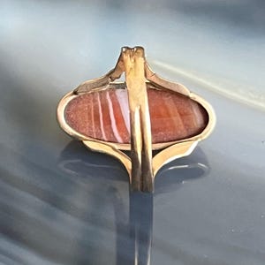 以下が含まれることがあります： 繊細な透かし模様に、赤と白の瑪瑙の石がセットされた金の指輪です。