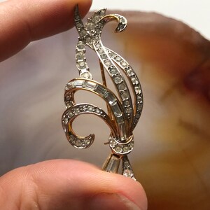 May include: A gold-toned brooch with a floral design, featuring clear rhinestones and baguette-shaped crystals.