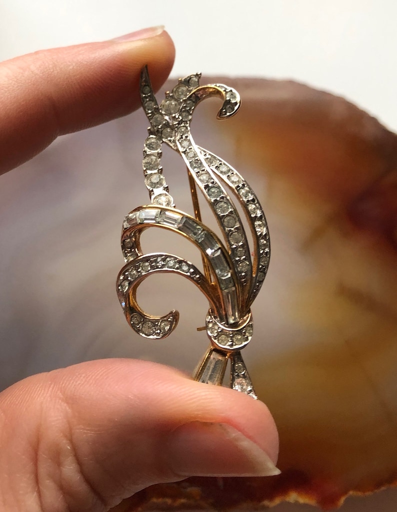 May include: A gold-toned brooch with a floral design, featuring clear rhinestones and baguette-shaped crystals.