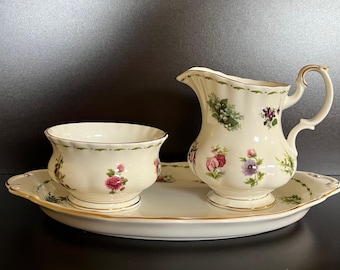 Puede incluir: Juego de servir de porcelana color crema con diseños florales. El juego incluye una jarra, un cuenco pequeño y una bandeja ovalada. El estampado floral presenta flores rosas, moradas y blancas con hojas verdes. Ribetes dorados.