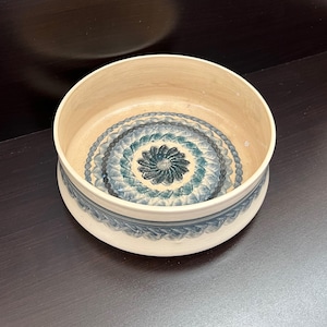 Peut inclure: Un bol rond en céramique crème avec un motif floral bleu et sarcelle détaillé à l'intérieur et sur le bord. Le bol a un design large et ouvert et une bordure décorative.