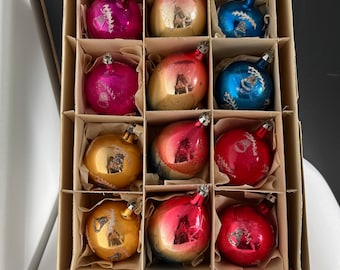 May include: A box of twelve vintage glass Christmas ornaments. The ornaments are in various colors, including gold, red, pink, and blue. The ornaments are in a cardboard box with individual compartments.