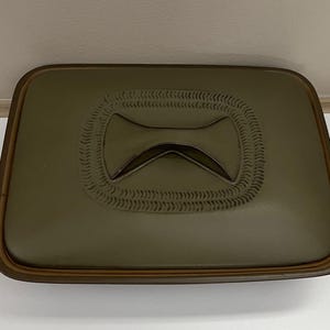 May include: An olive green rectangular ceramic dish with a decorative bow-tie design in the centre. The bow-tie is surrounded by a textured border. The dish has a brown rim.
