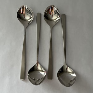 May include: Four stainless steel spoons with a reflective surface. The spoons have a rounded bowl and a long, slender handle. The spoons are arranged in a row against a white background.