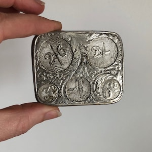 May include: Silver belt buckle with an intricate floral design and four engraved numbers: 1/6, 2/6, 3/6, and 4/6.