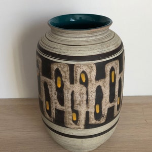 May include: A ceramic vase with a white, brown and yellow geometric pattern. The vase has a teal green rim and a white background.