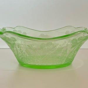 Könnte beinhalten: Eine hellgrüne Glasschale mit floralem Muster. Die Schale hat einen gewellten Rand und zwei Griffe. Die Schale ist etwa 25 cm breit und 10 cm hoch.