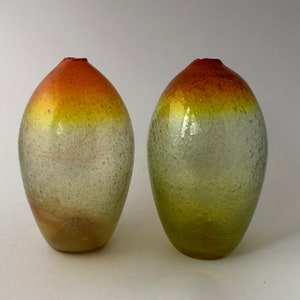 May include: Two glass vases with a textured surface. The vases are ombre, transitioning from a red to yellow to a light green color.