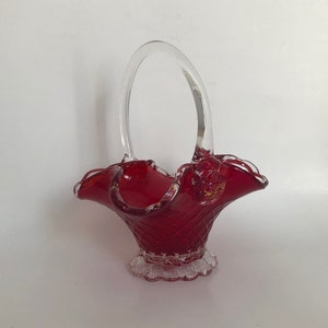 May include: A red glass basket with a clear glass handle. The basket has a scalloped edge and a textured design.