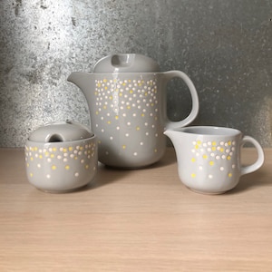 May include: A grey ceramic teapot, creamer and sugar bowl set with a white and yellow polka dot pattern.