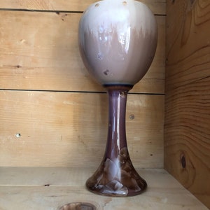 Pode incluir: Um vaso alto de cerâmica marrom e branco com uma base larga e redonda e um pescoço estreito. O vaso tem um desenho floral na base.