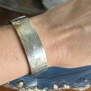 May include: A silver bangle bracelet with an engraved design of a bird and foliage.