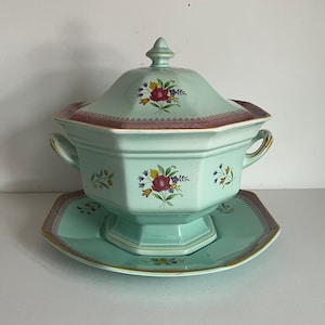 May include: A light blue porcelain soup tureen with a lid and a matching plate. The tureen has a floral design with pink, red, yellow, and purple flowers. The lid has a knob in the shape of a flower.