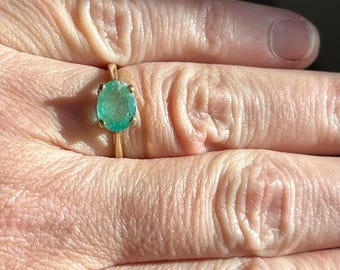 Peut inclure: Une bague en or ornée d'une émeraude verte ovale. L'émeraude est maintenue par quatre griffes, et le corps de la bague est en or uni. La bague est présentée sur un doigt, mettant en valeur la couleur et la clarté de la pierre. Le design est classique.