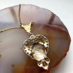May include: A gold pendant necklace with a detailed filigree design. The pendant is shaped like a teardrop and has a circular cutout in the center. The necklace is on a gold chain.