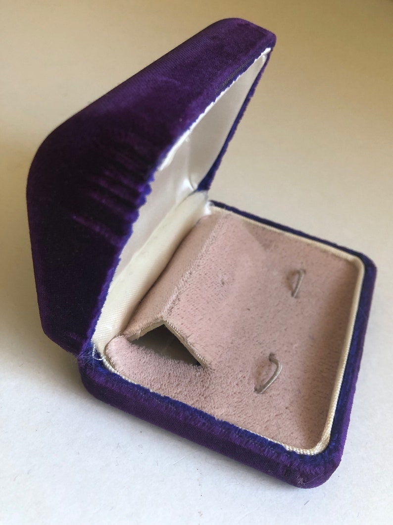 May include: A purple velvet jewelry box with a white satin interior and two small slots for earrings.