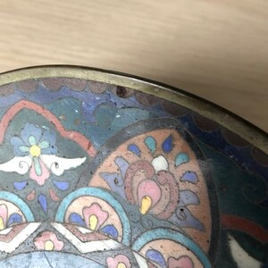 May include: A round, brass bowl with a colorful enamel design. The design features a floral pattern in shades of blue, pink, white, and yellow.