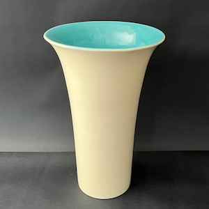 Könnte beinhalten: Eine cremefarbene Vase mit ausgestellter Form. Der Innenraum ist leuchtend türkisblau. Die Vase hat eine glatte, glänzende Oberfläche. Geeignet zur Präsentation von Blumen oder als dekoratives Element. Ungefähr 25 cm hoch.