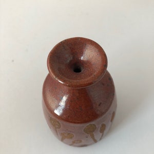 Puede incluir: Un peque&ntilde;o jarr&oacute;n de cer&aacute;mica marr&oacute;n con una abertura ancha y un acabado esmaltado. El jarr&oacute;n tiene un patr&oacute;n de manchas y l&iacute;neas marrones.