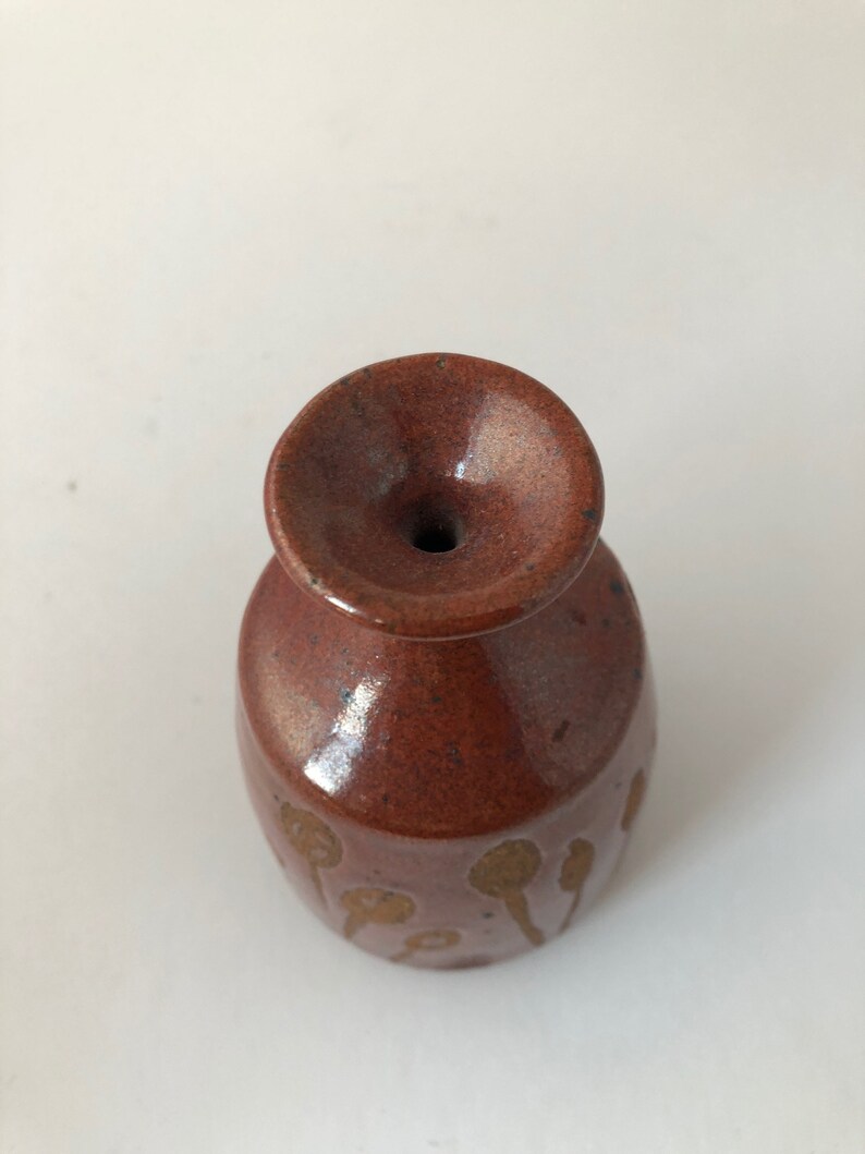 Puede incluir: Un peque&ntilde;o jarr&oacute;n de cer&aacute;mica marr&oacute;n con una abertura ancha y un acabado esmaltado. El jarr&oacute;n tiene un patr&oacute;n de manchas y l&iacute;neas marrones.