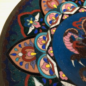 May include: A close-up of a decorative plate with a blue center and a colorful floral pattern around the edge. The plate is made of metal and has a glossy finish.