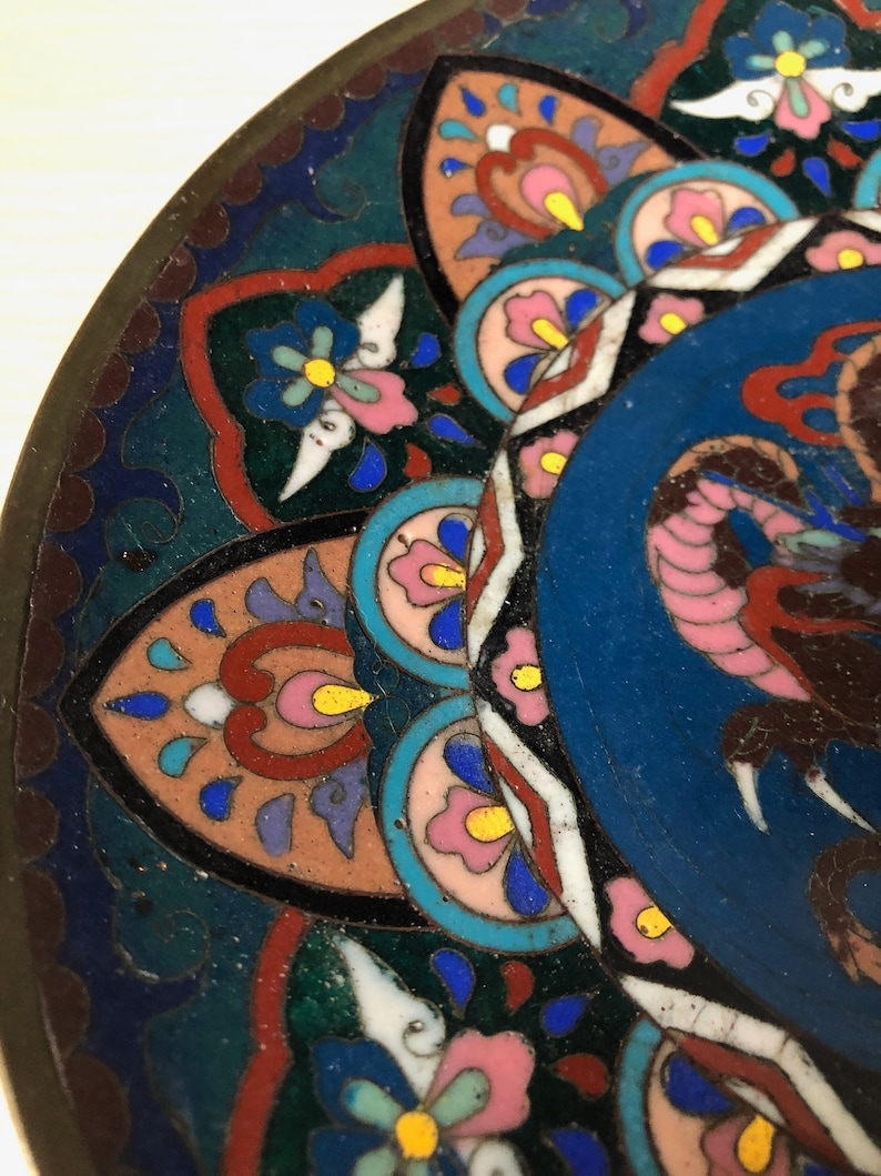May include: A close-up of a decorative plate with a blue center and a colorful floral pattern around the edge. The plate is made of metal and has a glossy finish.